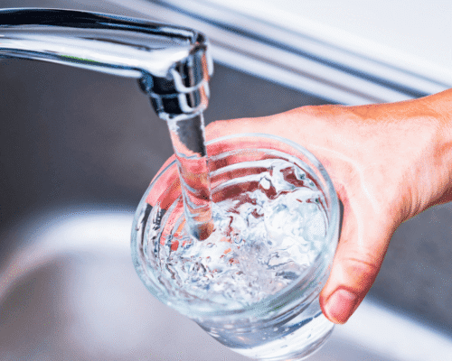 Hand holding glass under running kitchen faucet