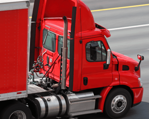 Bright red semi-truck driving on a highway, showing side view of cab and trailer