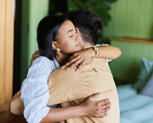 Woman embracing a grieving man in a warmly lit room, offering comfort during a moment of emotional distress.