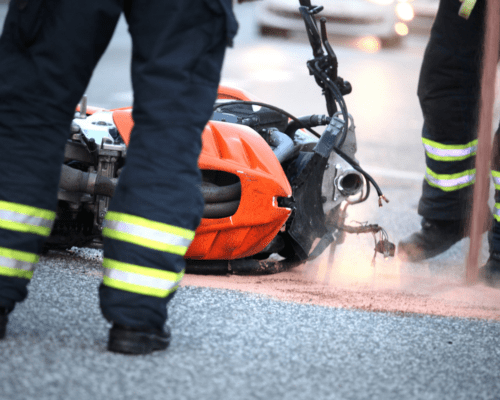 Emergency responders standing near a damaged motorcycle on a roadway, with debris and dust visible around the crash site. The image reflects the severity of motorcycle accidents in Savannah and highlights the potential for traumatic brain injuries, underscoring the importance of understanding legal options and pursuing compensation under Georgia law.