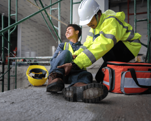 A construction site injury scene where a worker receives immediate assistance after a fall, emphasizing the critical role of proper safety equipment—such as fall protection systems and helmets—and how their absence can lead to serious workplace injuries and potential legal claims in Atlanta.