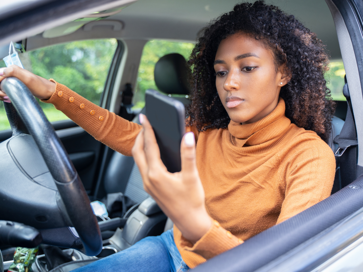Woman driving a car with one hand on the steering wheel and the other holding her phone.