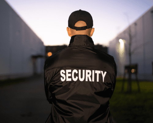 The back of someone wearing a security jacket and black hat.