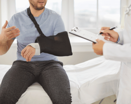 Injured man with his arm in a sling talking to a doctor taking notes on a clipboard, representing how to document a product defect injury in Georgia through medical records, preserved evidence, and liability documentation for a product liability claim.