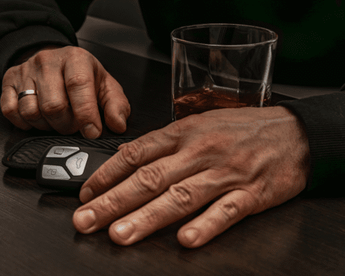 Close-up of a person’s hands resting near a car key fob and a glass of alcohol on a table. The image represents the dangers of drinking and driving and underscores the serious consequences that can lead to fatal DUI accidents and wrongful death claims in Savannah.
