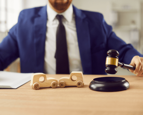 Attorney holding a gavel at a desk with two toy cars and documents, illustrating a car accident claim where initial insurance settlement offers in Savannah may undervalue damages and require negotiation for full compensation.